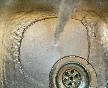 Wasser im Spülbecken Wasser fließt aus einem Wasserhahn in ein Spülbecken